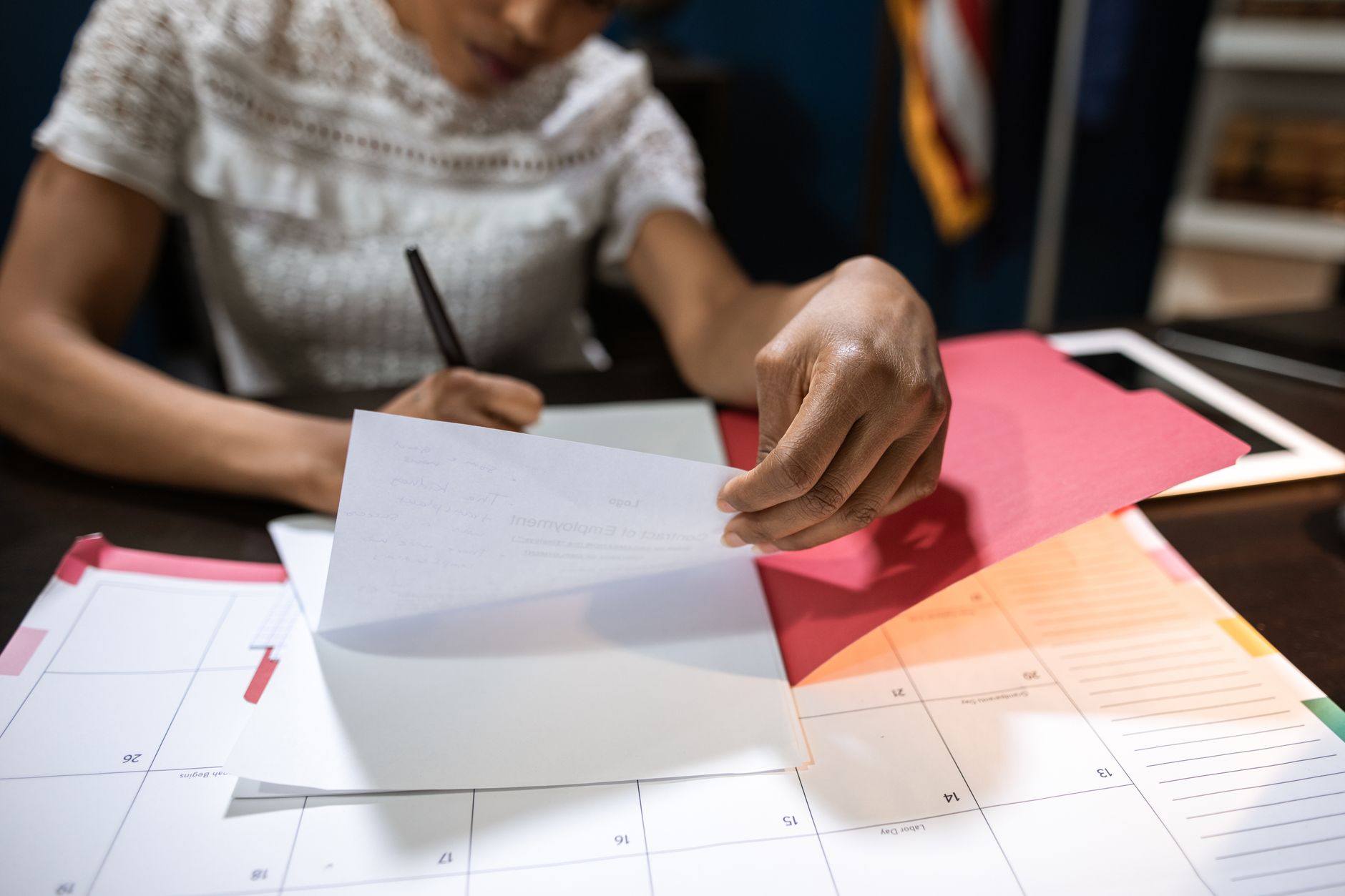Focused woman writing and organizing papers at a desk with a calendar.